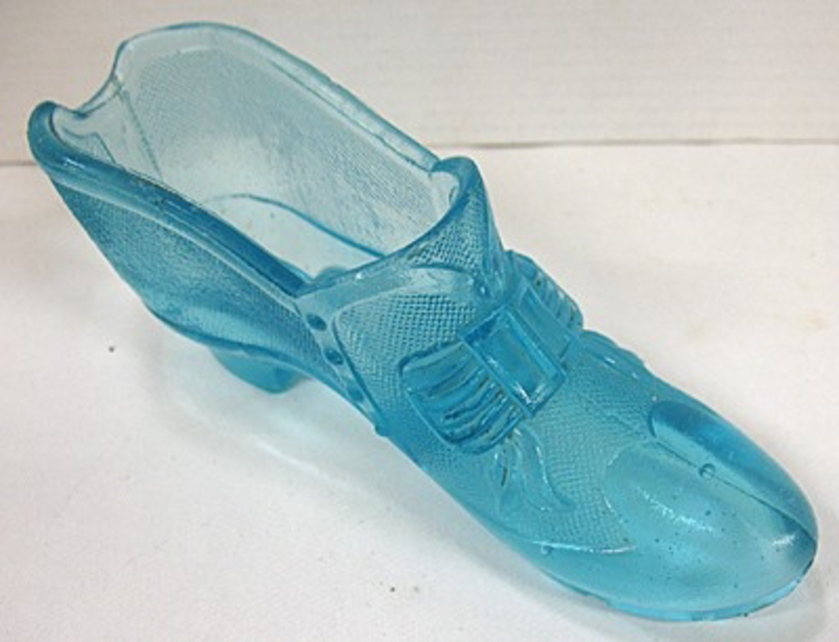 Ett par prydnadsskor av pressat glas.

Enligt givarna kallade ''Lyckans skor''. Skorna har inpressat i glaset en rosett ovantill samt knäppning i sidan. Skorna stod i givarnas barndomshem.

Ursprungligen användes sådana här skor som cigarrställ.