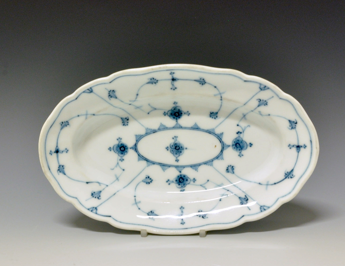 Avlangt fat av porselen. Bølget kant. 
Dekor: Stråmønster i blått
Modell:180.6 Facon Meissen
Finnes i priskuranten for 1905.