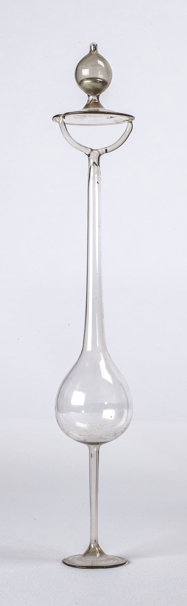 Tynt glassrør med håndtak, fot og en glassbalong på midten.