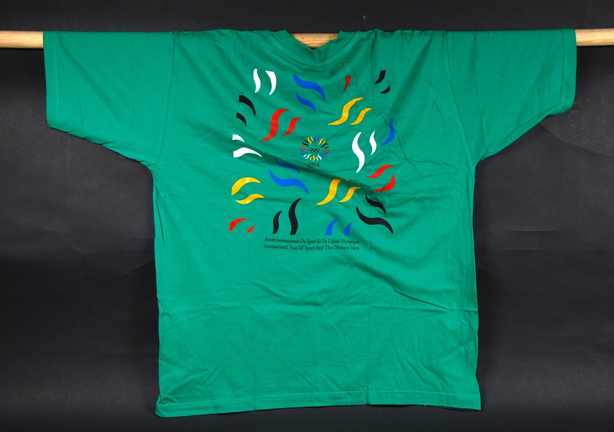 Grønn t-skjorte med to flerfargede logoer for "International Year Of Sport And The Olympic Ideal". T-skjorten er i størrelse XL.