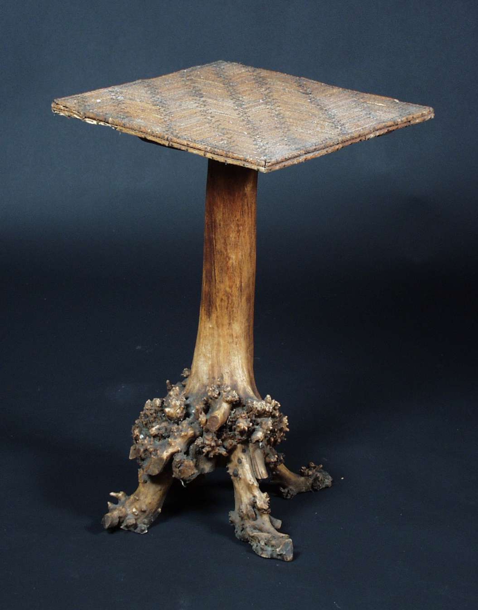 Et firkantet kubbebord som er lagd av furu og bjørk.
Bordplaten er lagd av furu med spikret furuskudd på overflaten. Bordbenet er stammen av en bjørk med utvekster.