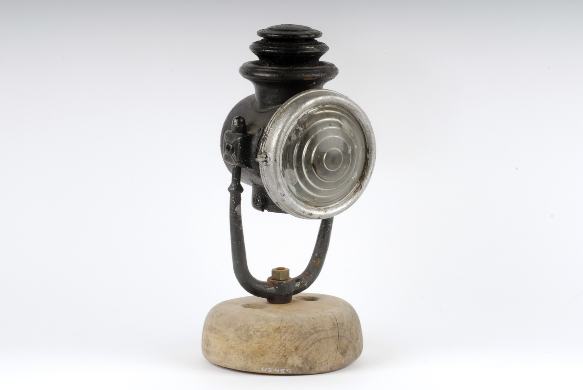 Form: Sylinderformet lykt med rundt glass i fronten.
Stativ av jern satt ned i foten. Oljedrevet til lampe før 1914 i Tyskland