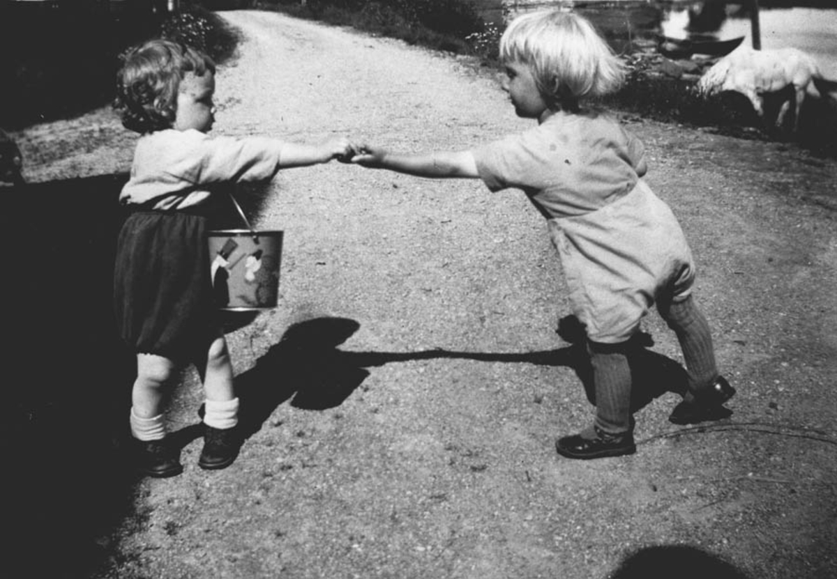 To små barn som leker sammen på en vei, ene har et lekespann.