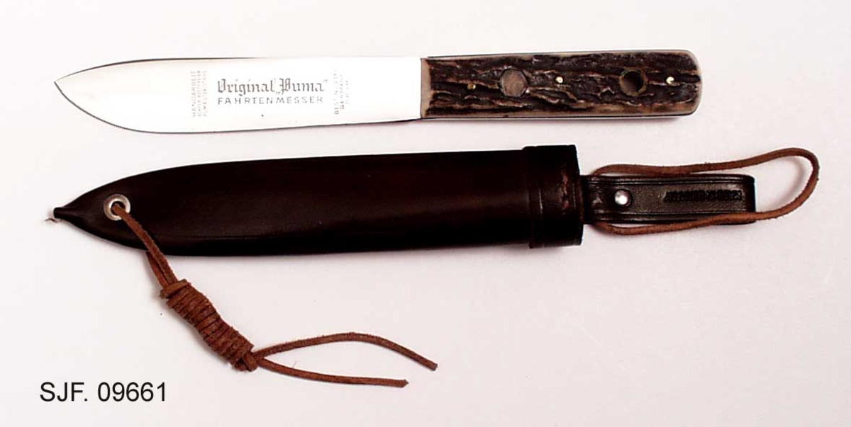 Kniven sitter fast i slira ved at et hull i knivskaftet hvor det er tredd ei reim som er festet til slira. 