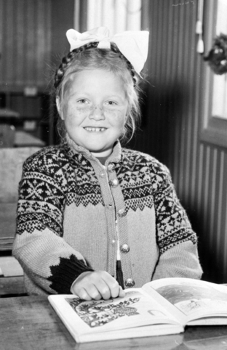 Åse Bratengen (Sameien) ved skolepulten i første klasse på Mauset skole, Brumunddal. Skolebok, strikkejakke, sløyfe i håret.