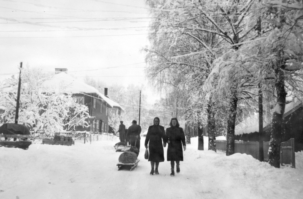 Moelv sentrum, to menn drar kjelke med varer. To ukjente kvinner, vinter. 