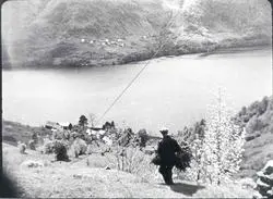 Havrå.Løypestreng. mann. klyngjetun. fjord. Nokre gardar i bakgrunnen. bratte lier. nokre tre.