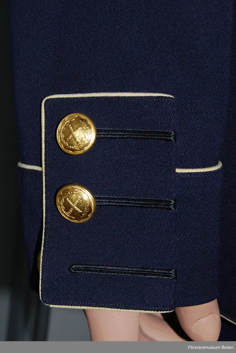 Mörkblått kläde, framtill dubbla rader med 8 knappar av Generalstabens modell. Krage med guldgalon runt kanten och tre metallstjärnor betecknande överste. Gula passpoaler (nu blekta till närmast vit färg) och gult foder. Tygklädd knapp och slejf vid vänstra axeln. Raka ärmuppslagsklaffar med blinda knapphål. Släpspänne för Svärdsorden sitter monterat på bröstet.