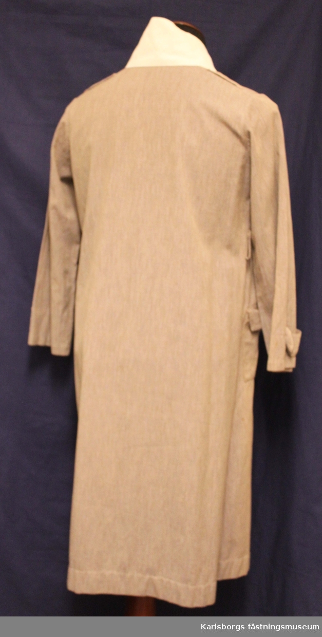Rockklänning för armélotta m/1923. Dubbelknäppt fram, utanpåsydda sidfickor med lock o knapp. Vit påknäppbar krage samt manschetter.