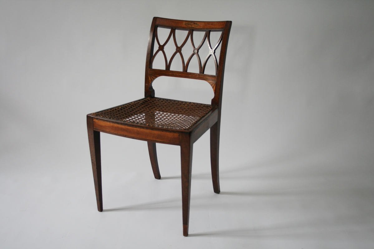 En av 4 mahogny stoler med intarsia; skjell dekor og vifte form. Ryggbrikke skåret ut i fire x-er med en runding i midten. Rotting sete.