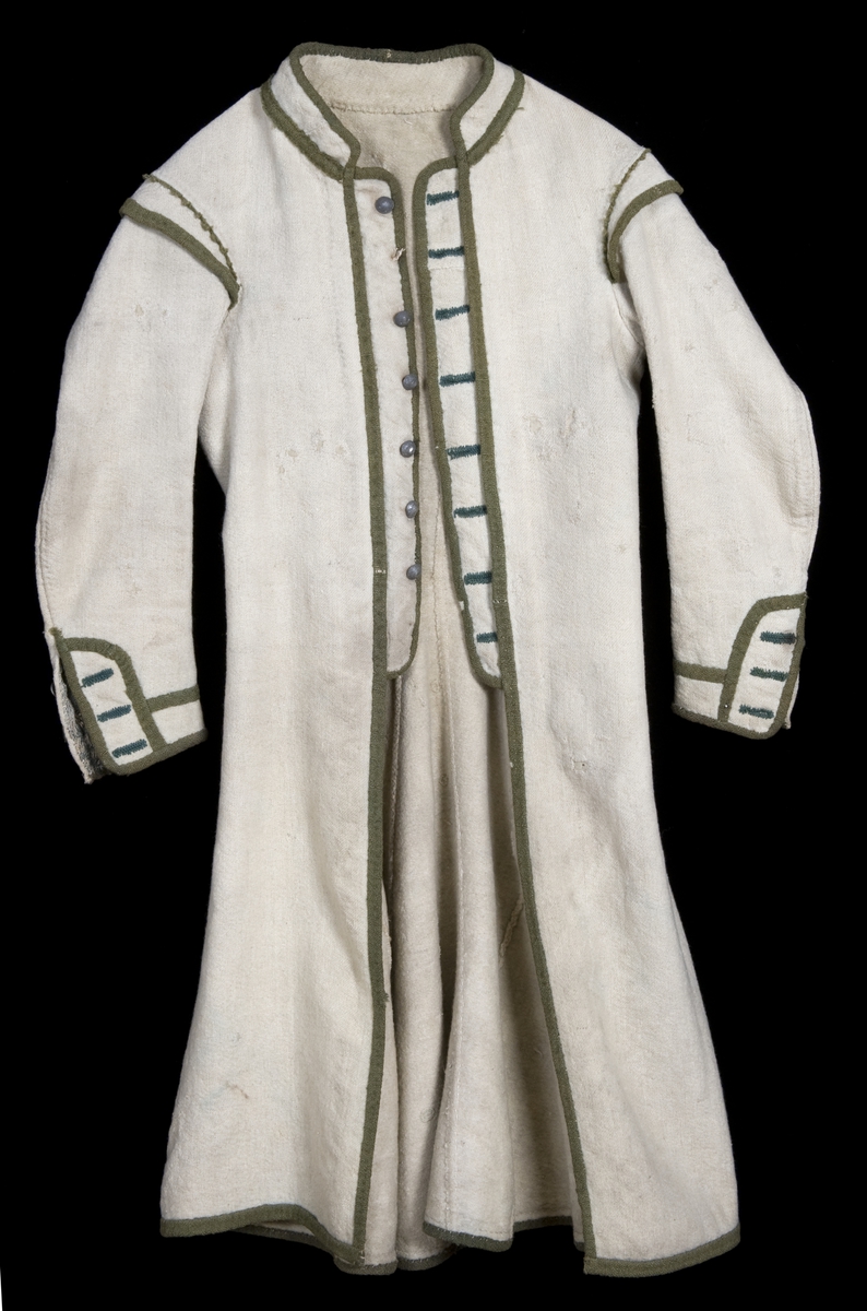Hvit kjole av ull med grøn dekor av ull.
Midjen bak er markert med to garn dusker.