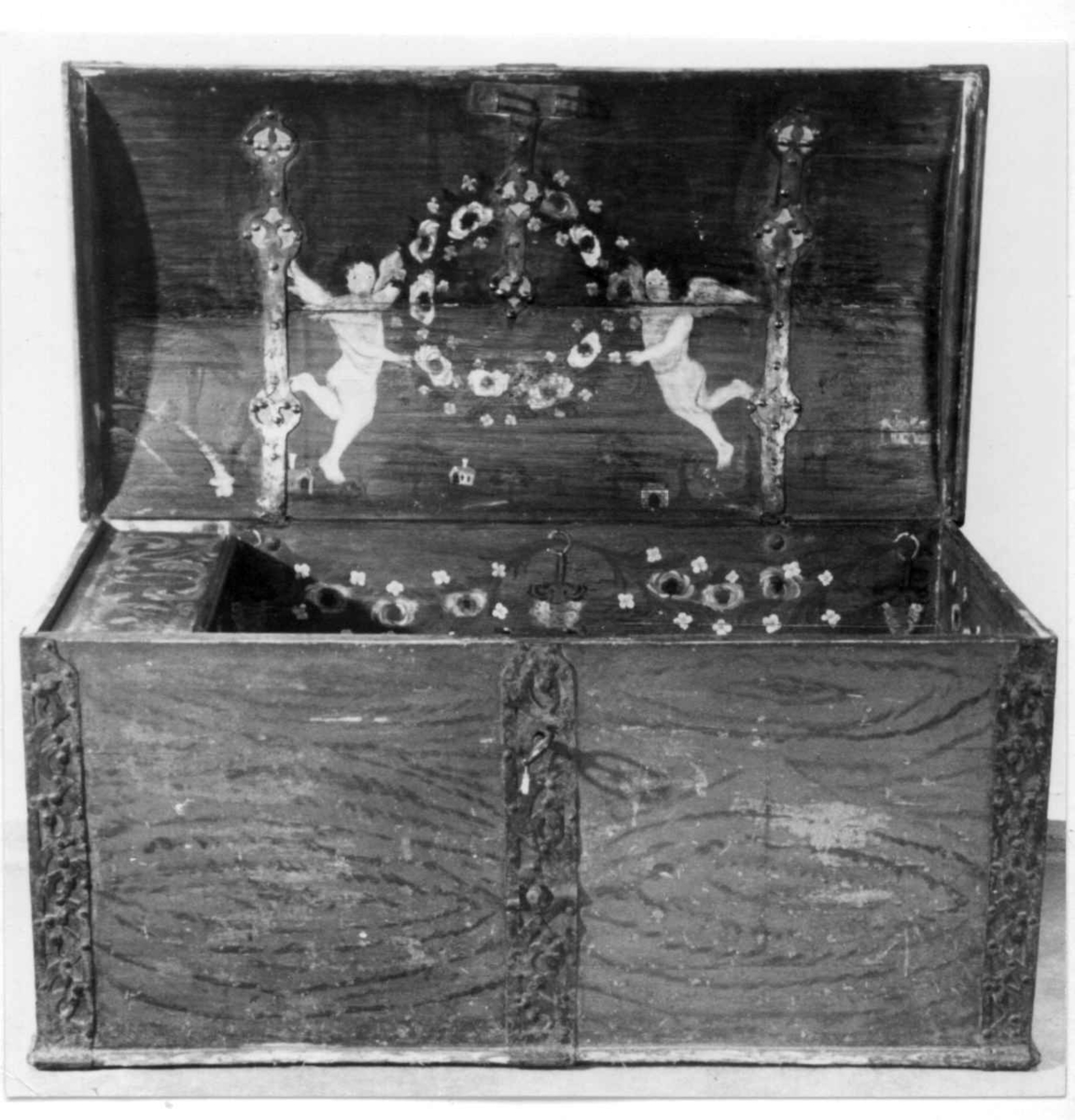 Kiste med buet lokk og gjennombrudte jernbeslag og bånd. Utvendig ådret og med initialer og årstall på baksiden. Innvendig bemalt med to engler og små hus i lokket.