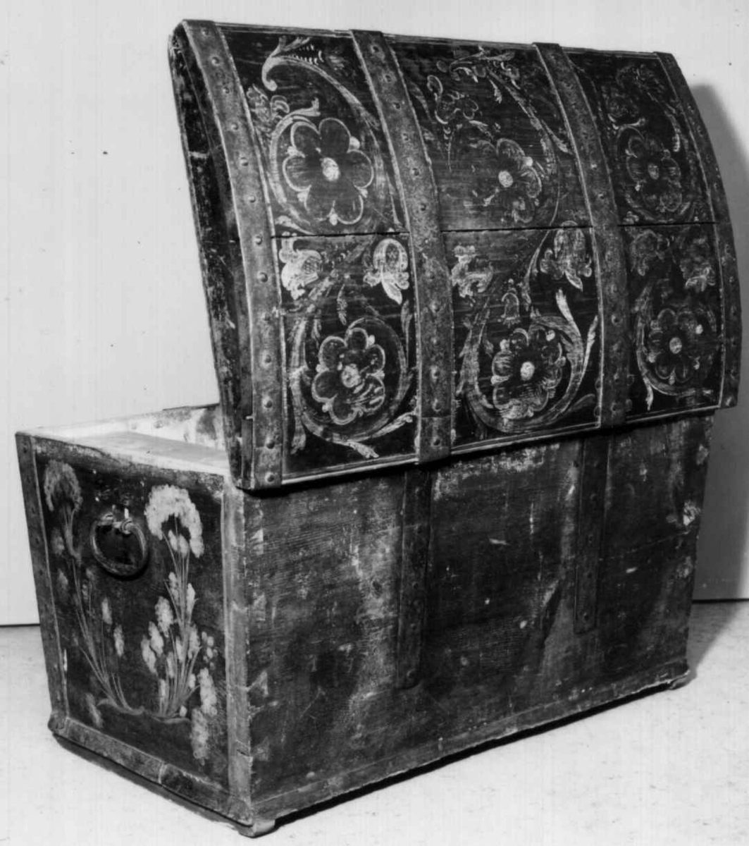 Kiste med buet lokk og smijernsbeslag og bånd. Rosemalt lokk og tre sider. innvnedig bemalt og med leddik. Kisten har små føtter.