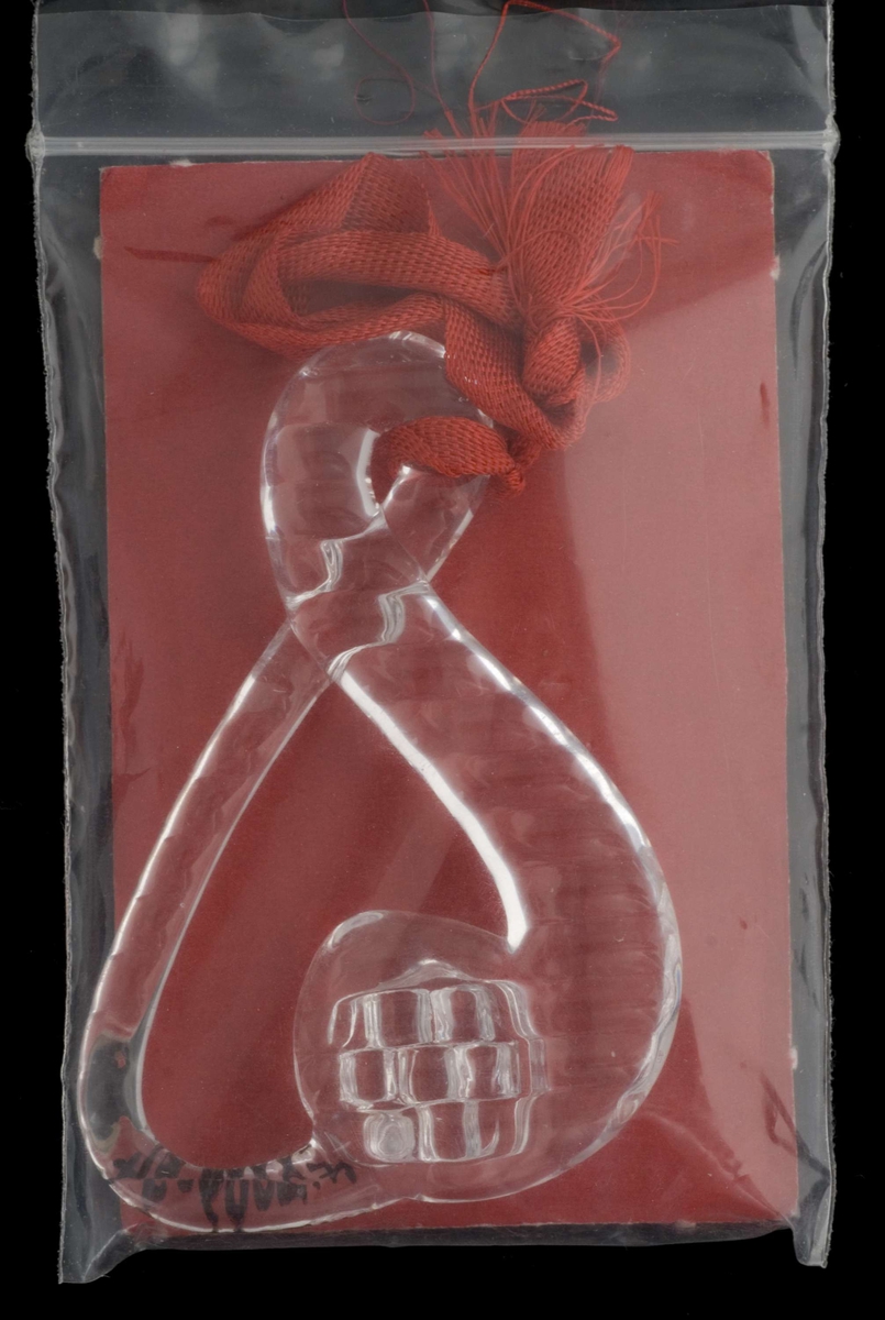 s-formet juletrepynt i klart glass med rød silkesnor. Ligger i gjennomsiktig plastpose.
