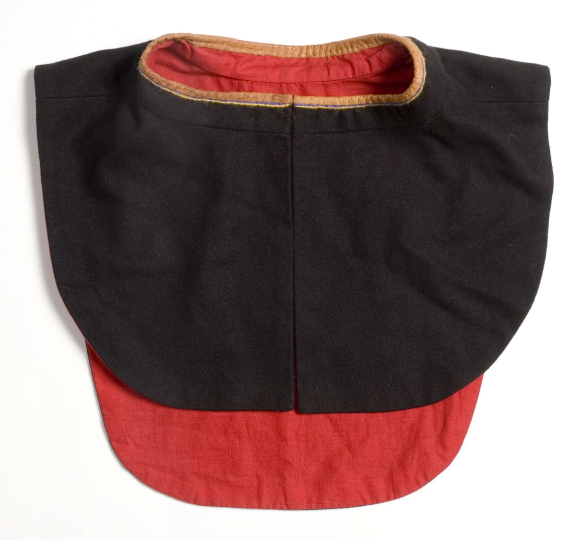 Brystklede til samisk mannskofte NFSA.4458A, av svart klede kantet med brunt skinn og brodert med rødt, gult og blått med innlagte stykker av kråkesølv. Foret med rødt tynt stoff. Festes med sikkerhetsnål.