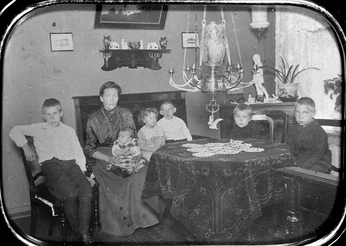 Stueinteriør med kvinne og 6 barn, Stoler, sofa, bord, kommode, gardiner. Vogtsgt., Oslo, ant. 1911