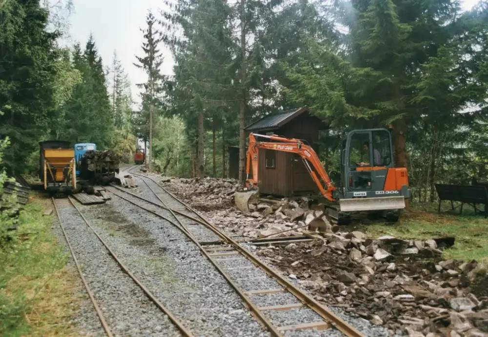 En oransje gravemaskin graver ved siden av en skinnegang.