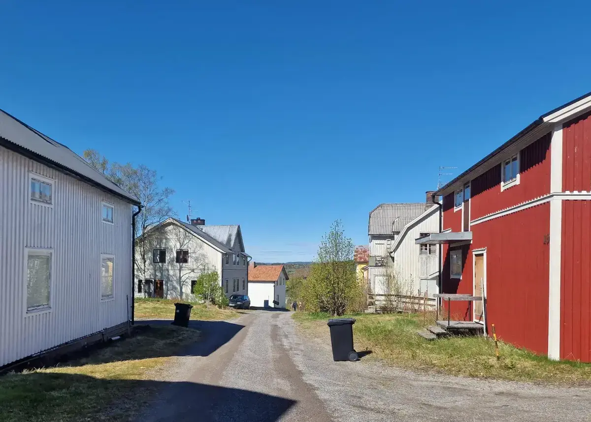 Grusväg med hus som står efter vägen, samt soptunnor.