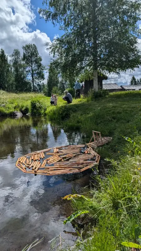 En miniatyrutgave av spillflåte med tømmerlense ligger i dammen på bygdetunet. 
