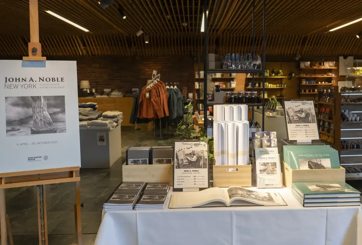 Bord med bøker, plakater og produkter knyttet til utstillingen «John A. Noble – New York i stein og saltvann» i museumsbutikken.